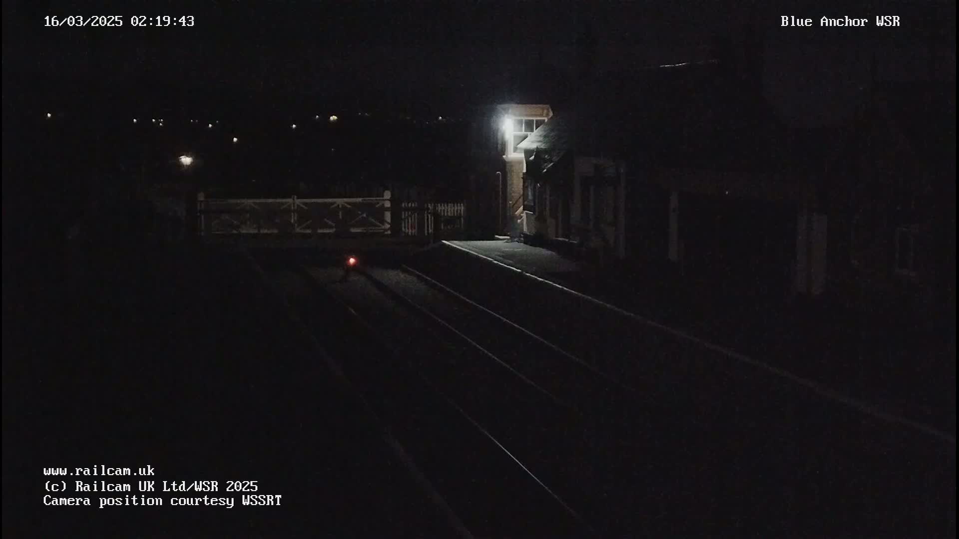 A nighttime view of a dimly lit train station platform with train tracks and a building.