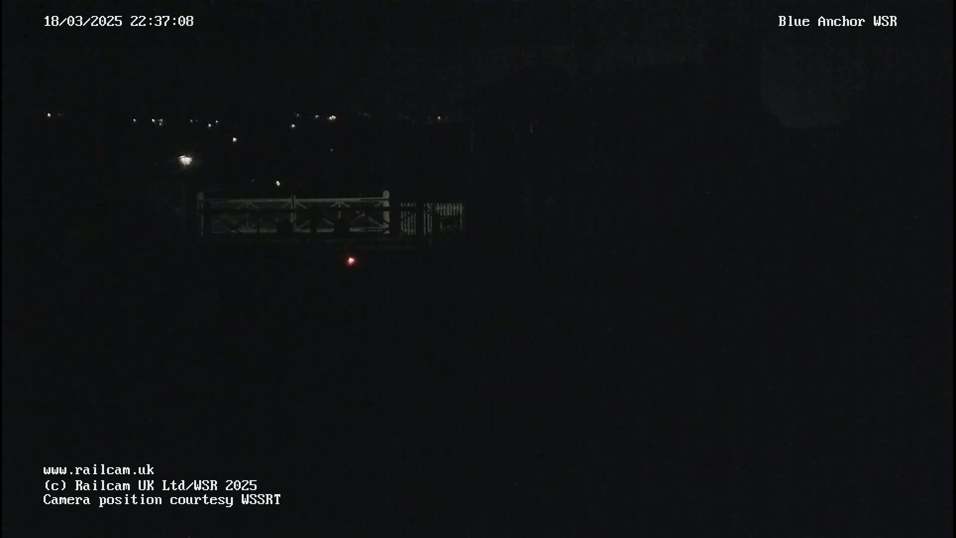 A nighttime, dark view of a bridge with faint lights in the distance.