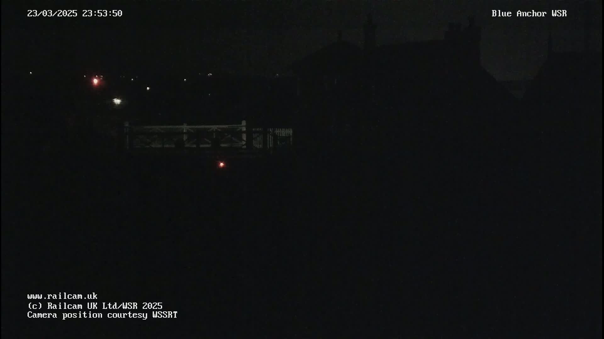A nighttime view shows a dark silhouette of a building and a bridge under a dark sky.