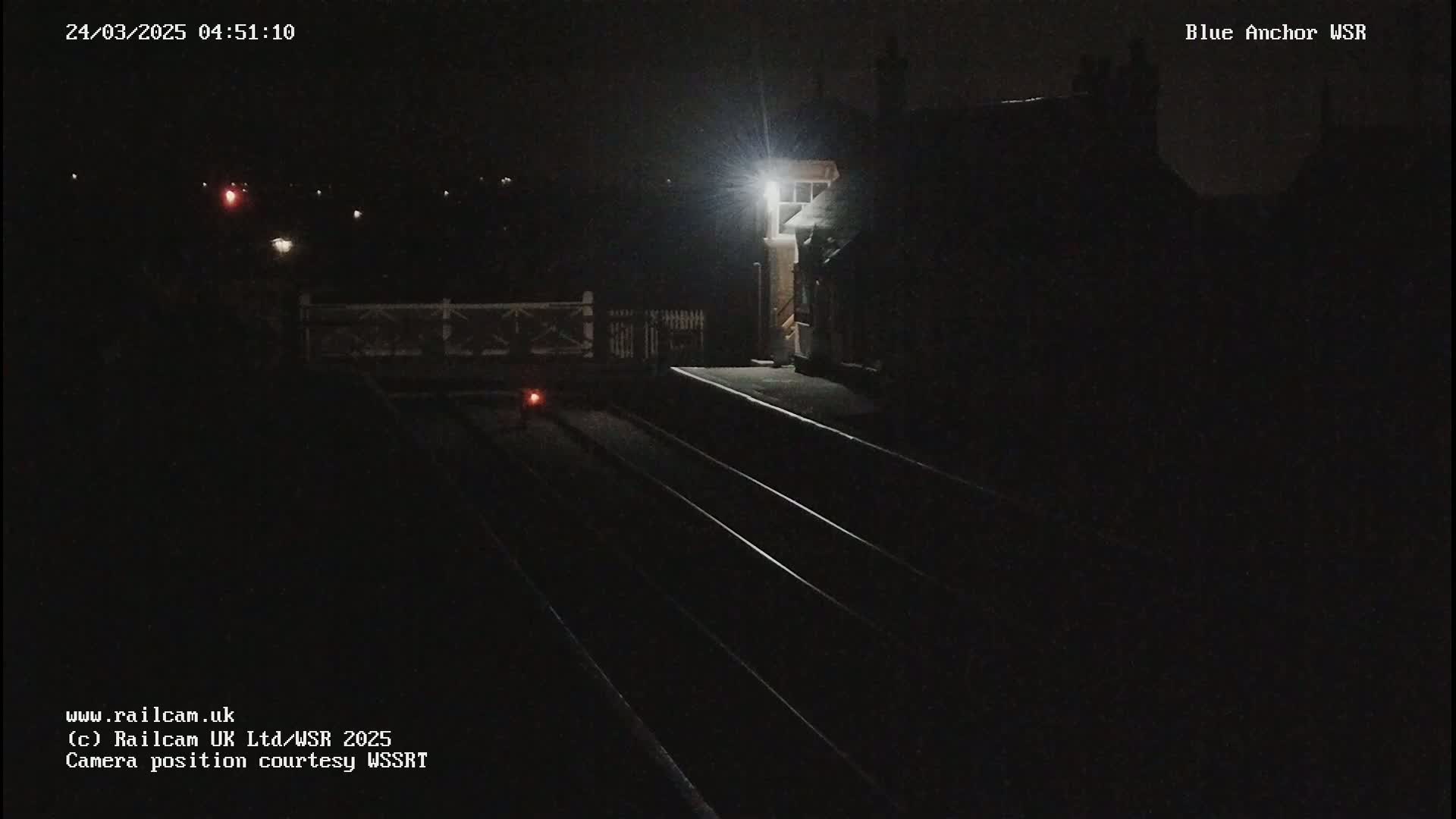 A nighttime view of a dimly lit train station platform with three train tracks and a signal light.