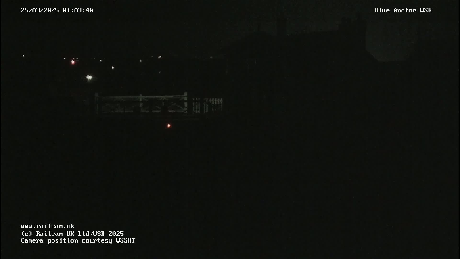 A dark, nighttime view of a bridge and distant buildings under a clear sky.