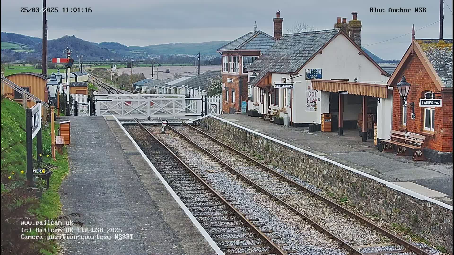 A railway station with several buildings and train tracks under an overcast sky.