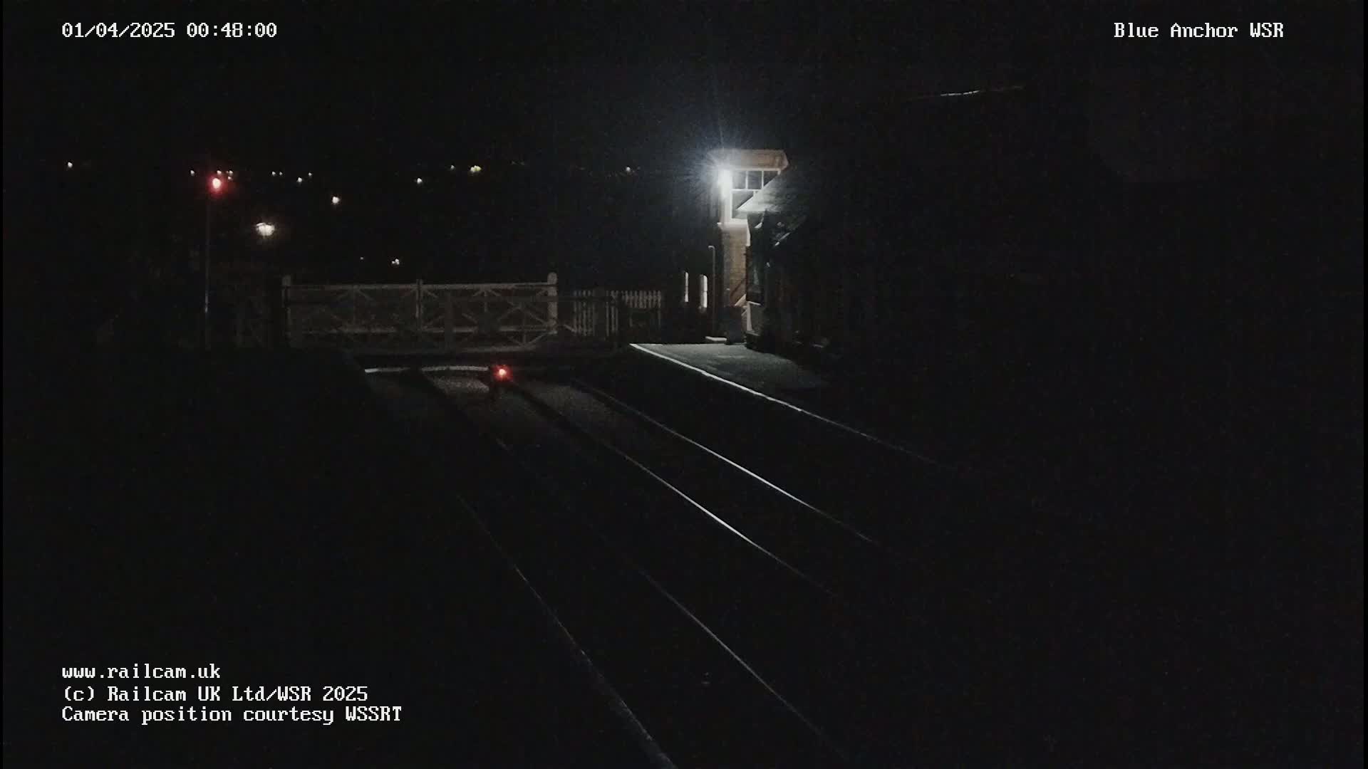 A nighttime view of train tracks and a dimly lit station platform under dark conditions.