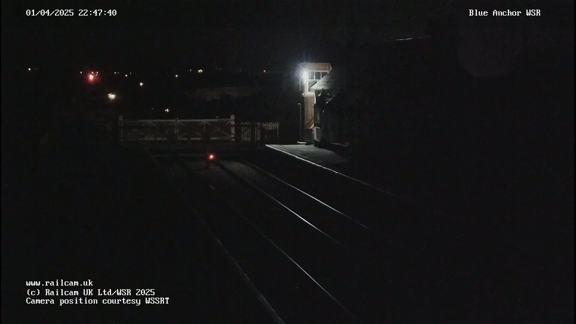 A nighttime view of a dimly lit train station platform with three sets of train tracks.