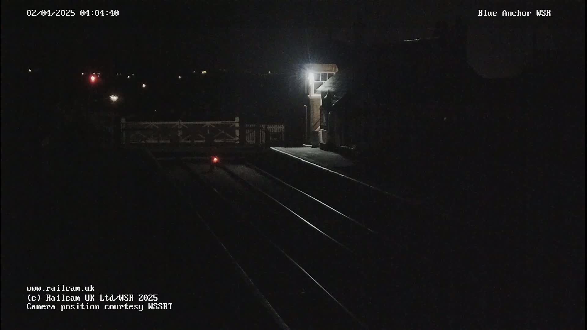 A dark nighttime view of train tracks and a dimly lit station building.