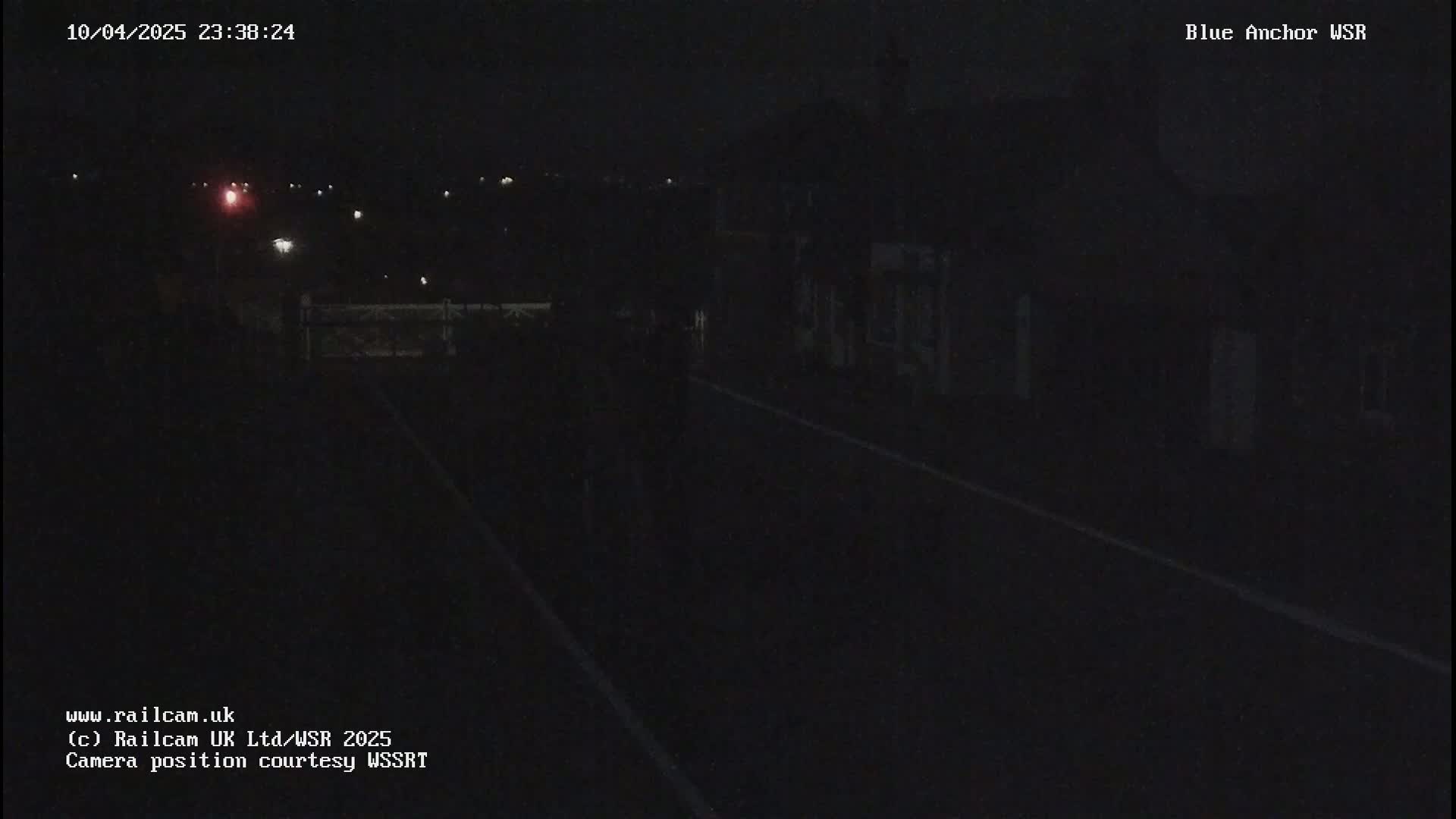 A dark, nighttime view of a road and buildings, with some distant lights visible.
