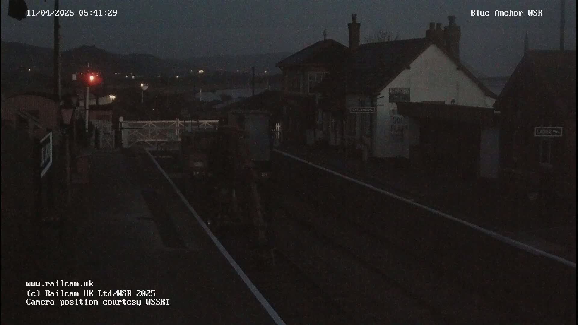 A dark, nighttime view of a train station with a train approaching under a dusky sky.