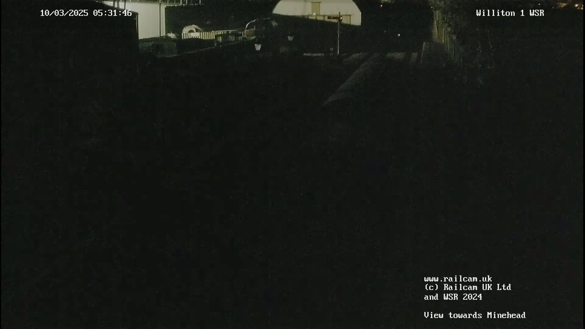 A dark, nighttime view of a dimly lit area, possibly a train yard or similar industrial setting.