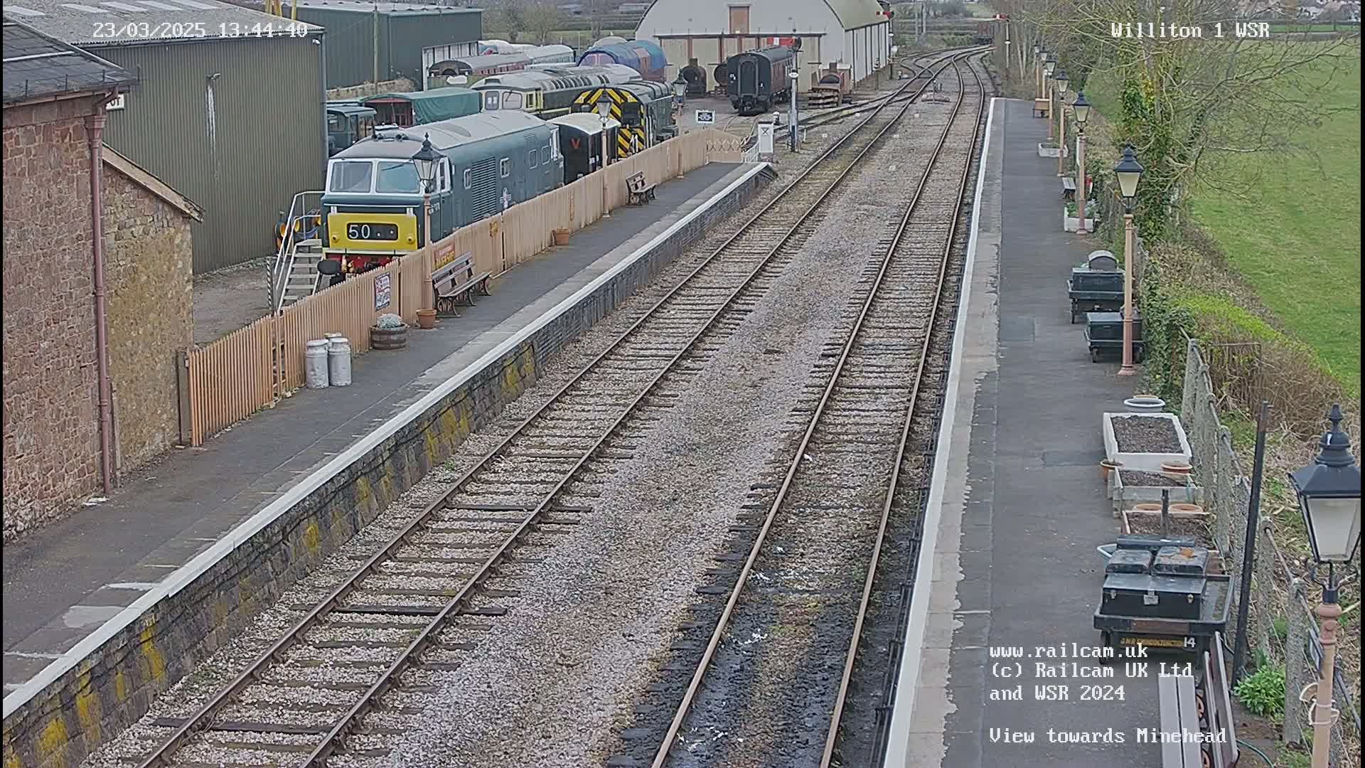 A train station platform with multiple train cars and tracks, under a partly cloudy sky.