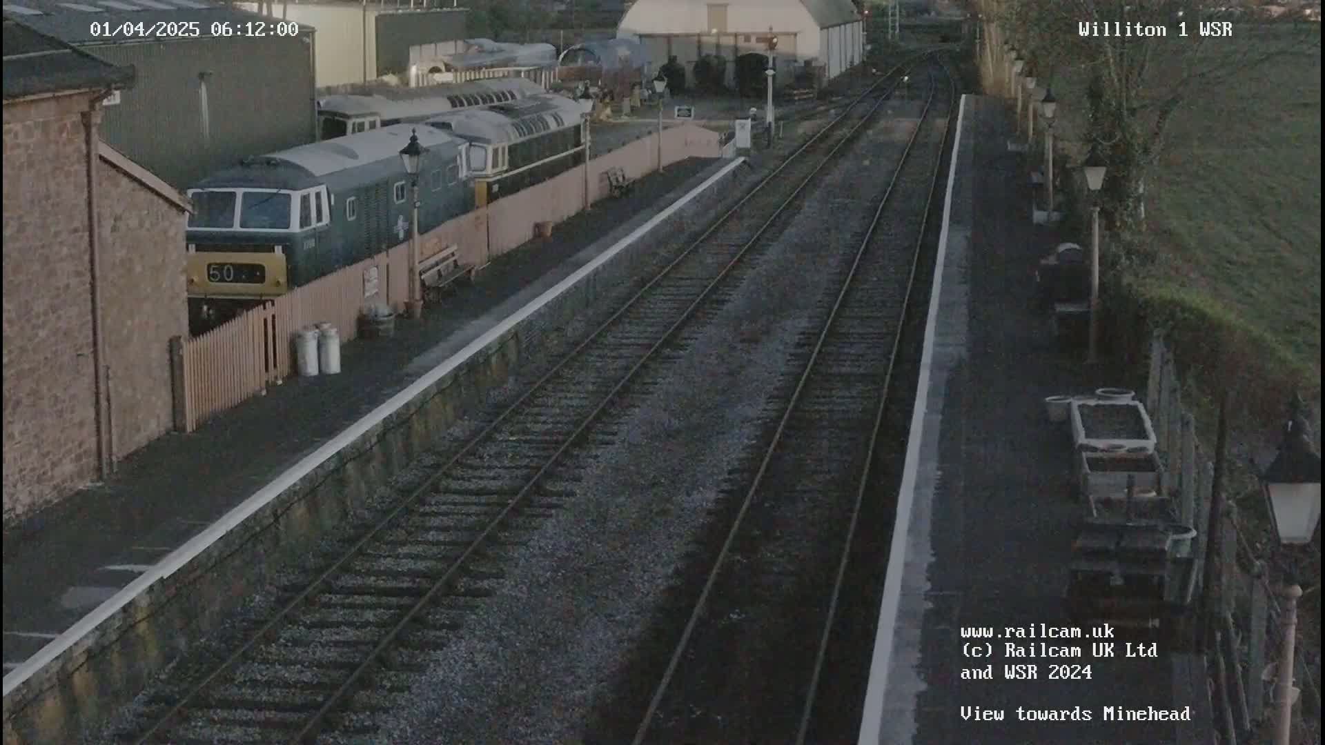 A train and several rail cars sit in a station yard on a gloomy morning.