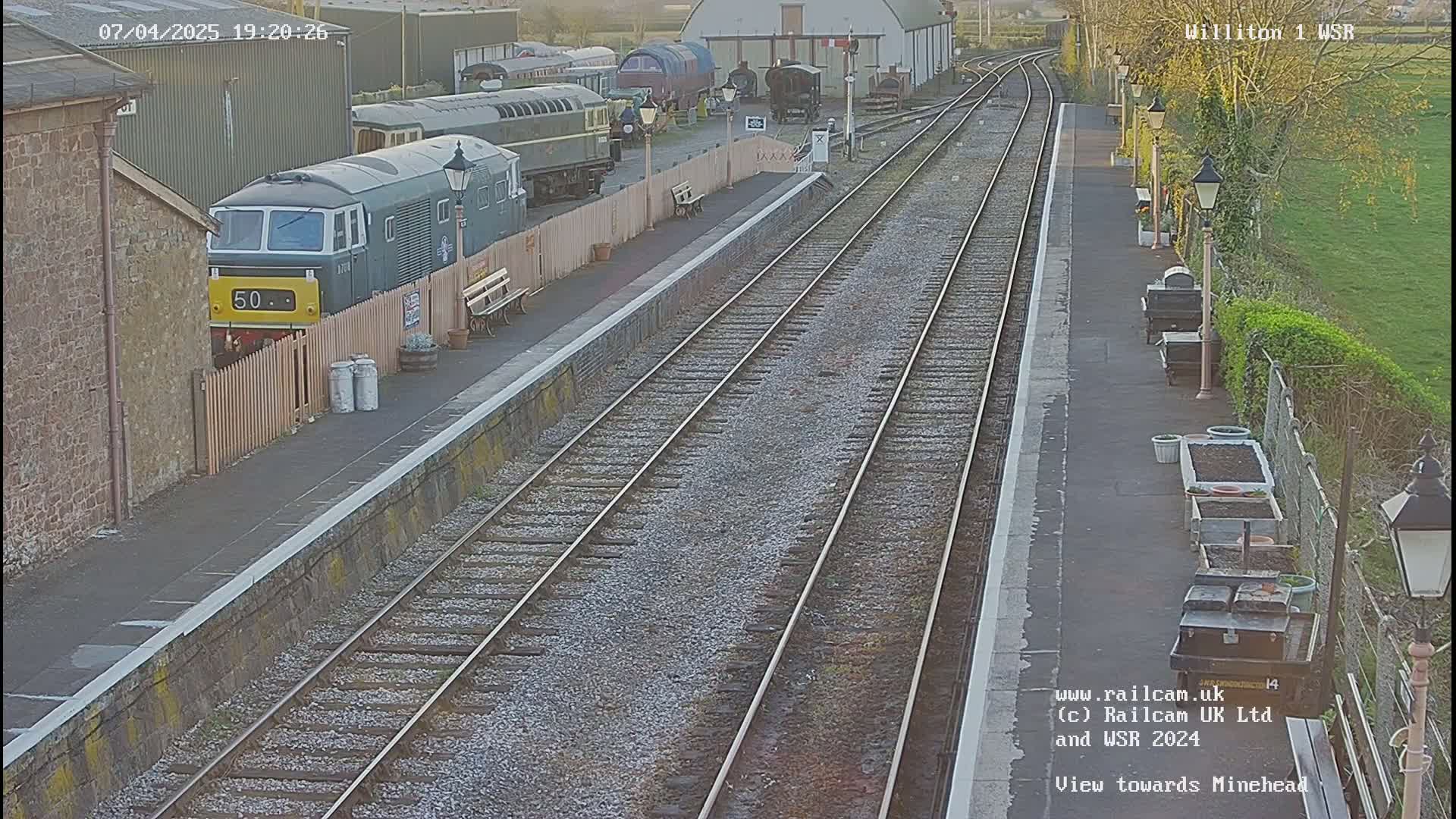 A train sits at a railway station platform on a partly sunny evening.