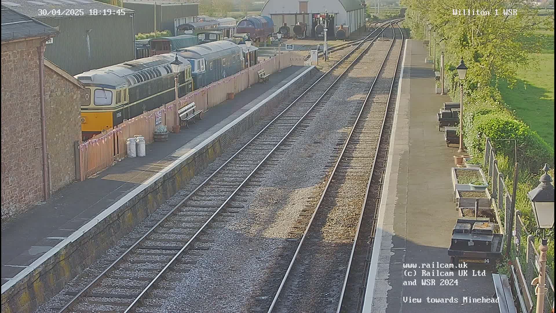 A train station platform with multiple train tracks and several trains parked nearby on a sunny day.