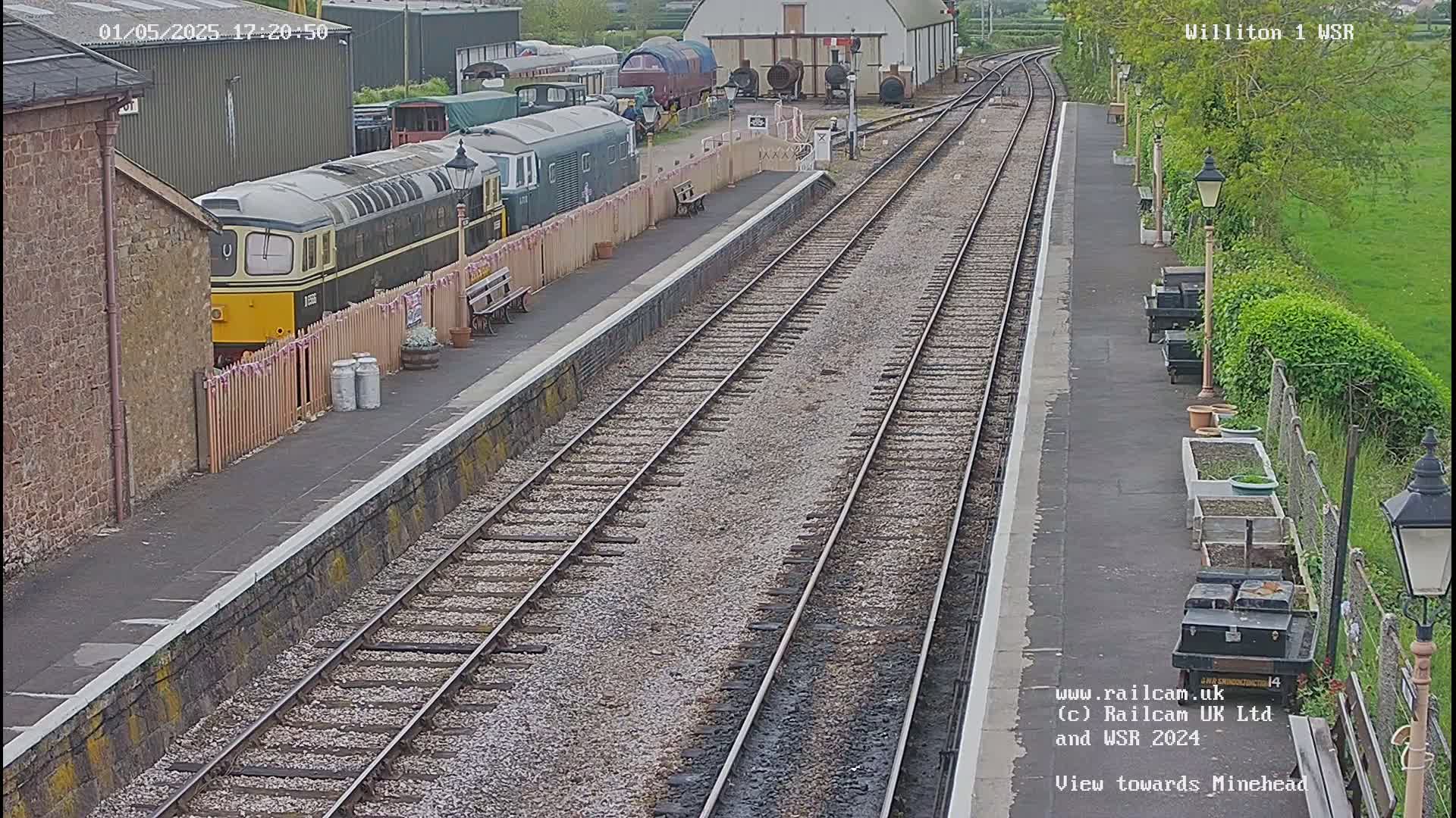 A railway station with a diesel locomotive parked next to a platform, viewed from above on an overcast day.