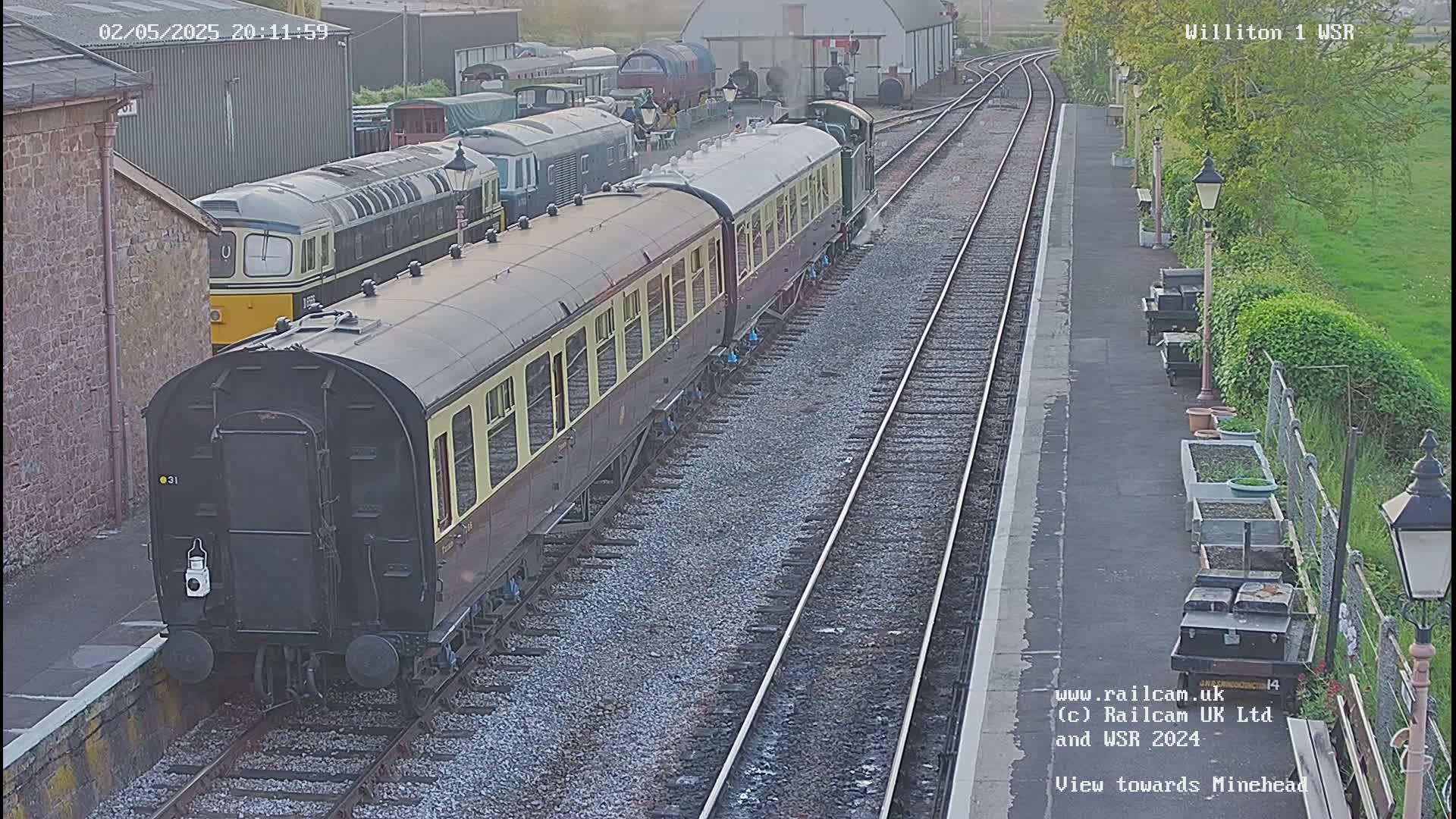 A passenger train is parked at a railway station under a twilight sky.