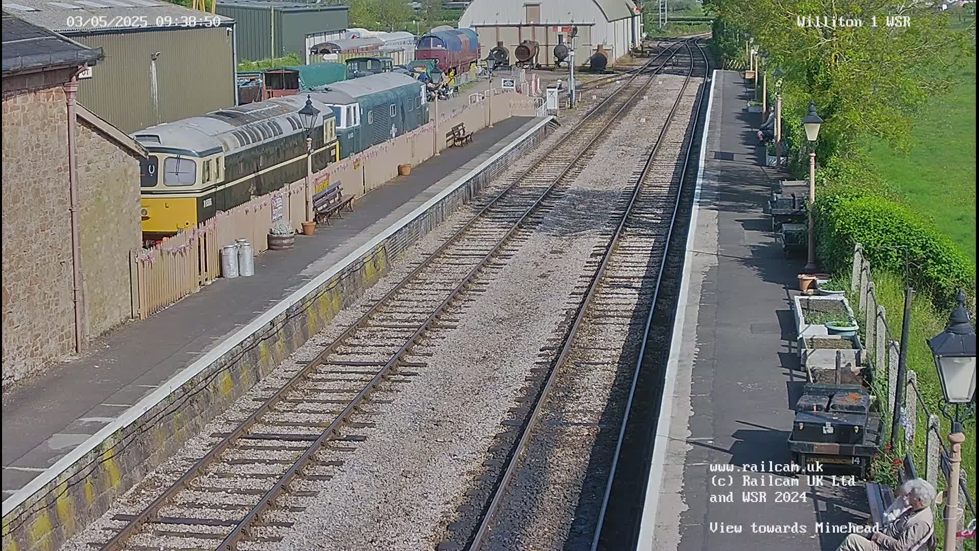 A sunny day at a train station with multiple train cars and tracks, including a diesel locomotive parked at a platform.