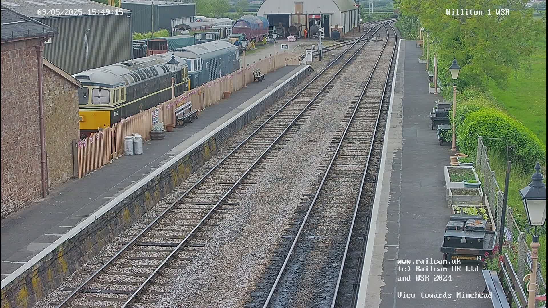 A railway platform with multiple train cars and tracks, viewed on a partly sunny day.