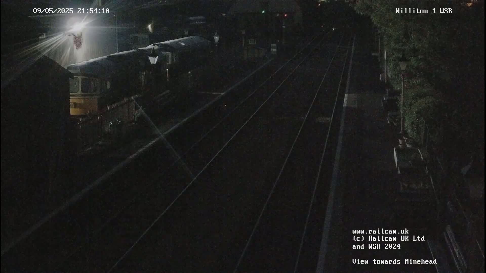A train sits at night in a dimly lit train station next to train tracks.