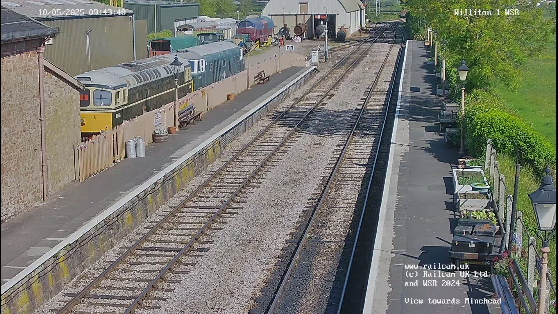 A sunny day at a train station with multiple railway tracks, a diesel locomotive, and other railway cars parked nearby.