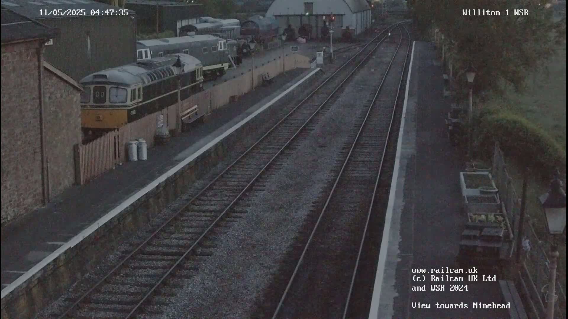 A train sits at a dimly lit railway station platform under a twilight sky.
