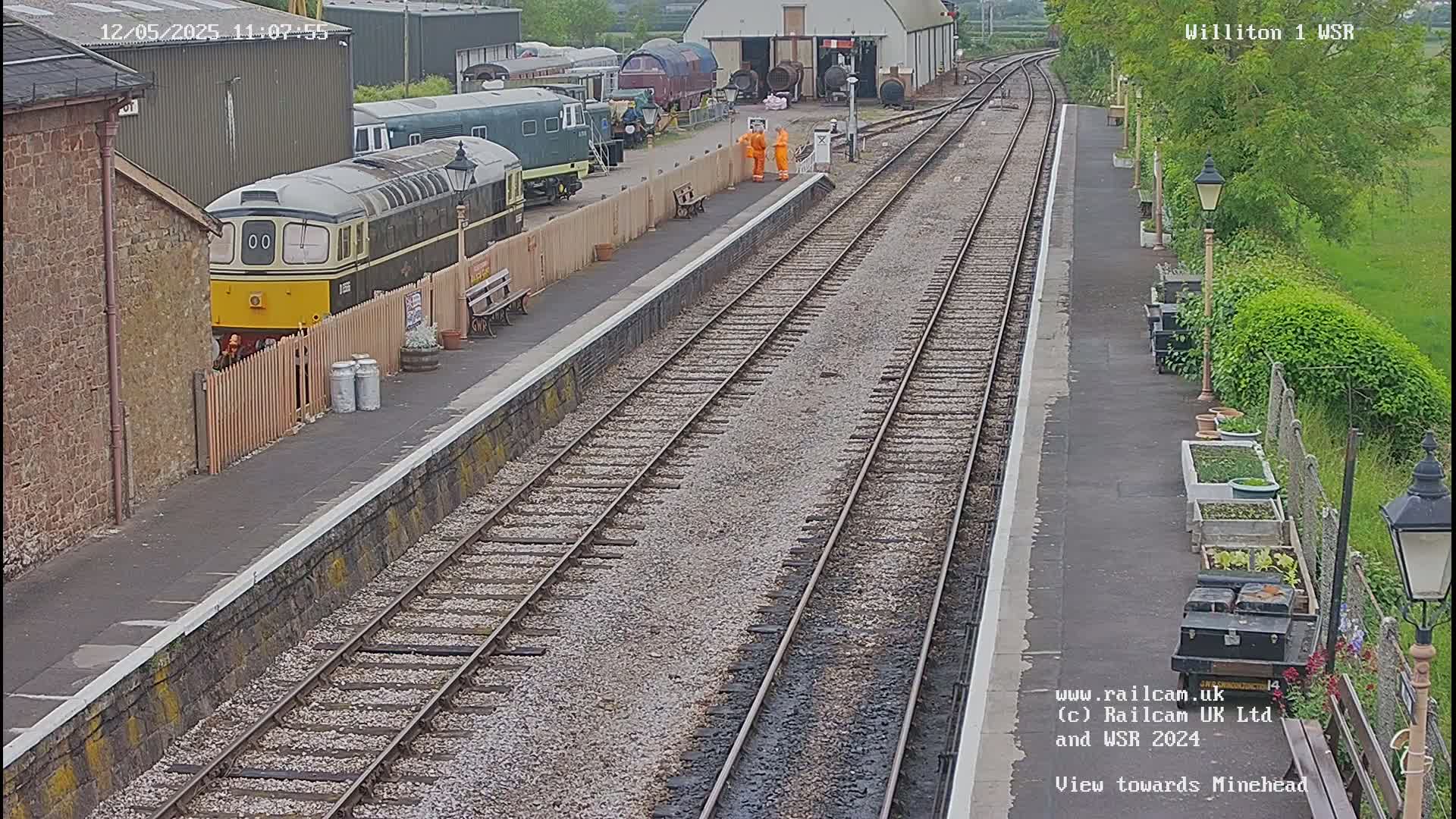A train sits at a station platform next to several other train cars, under a partly cloudy sky.