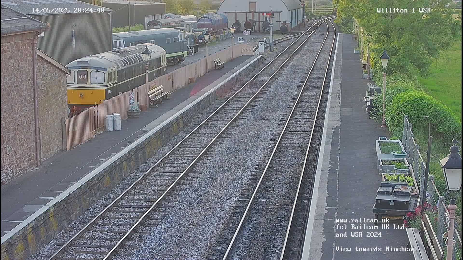 A diesel locomotive is parked at a train station on a partly sunny evening, with multiple train tracks extending into the distance.