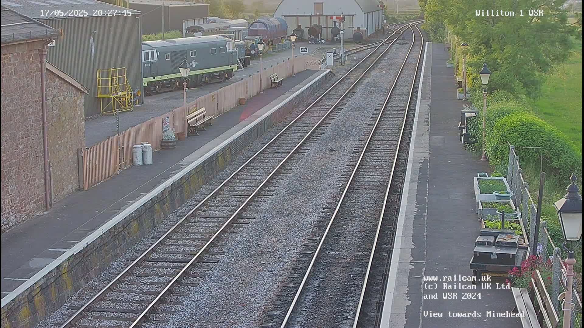 A train station platform with two train tracks extends into the distance under a twilight sky.