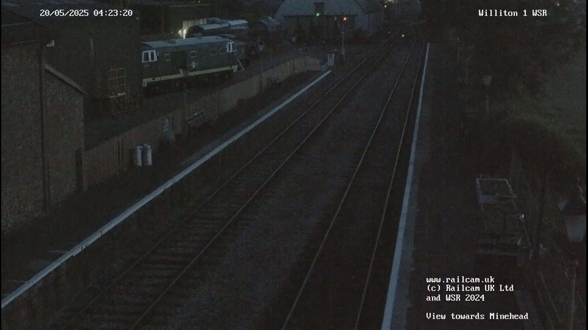 A nighttime view of a train station with railway tracks extending into the distance, showing a train parked near a building.