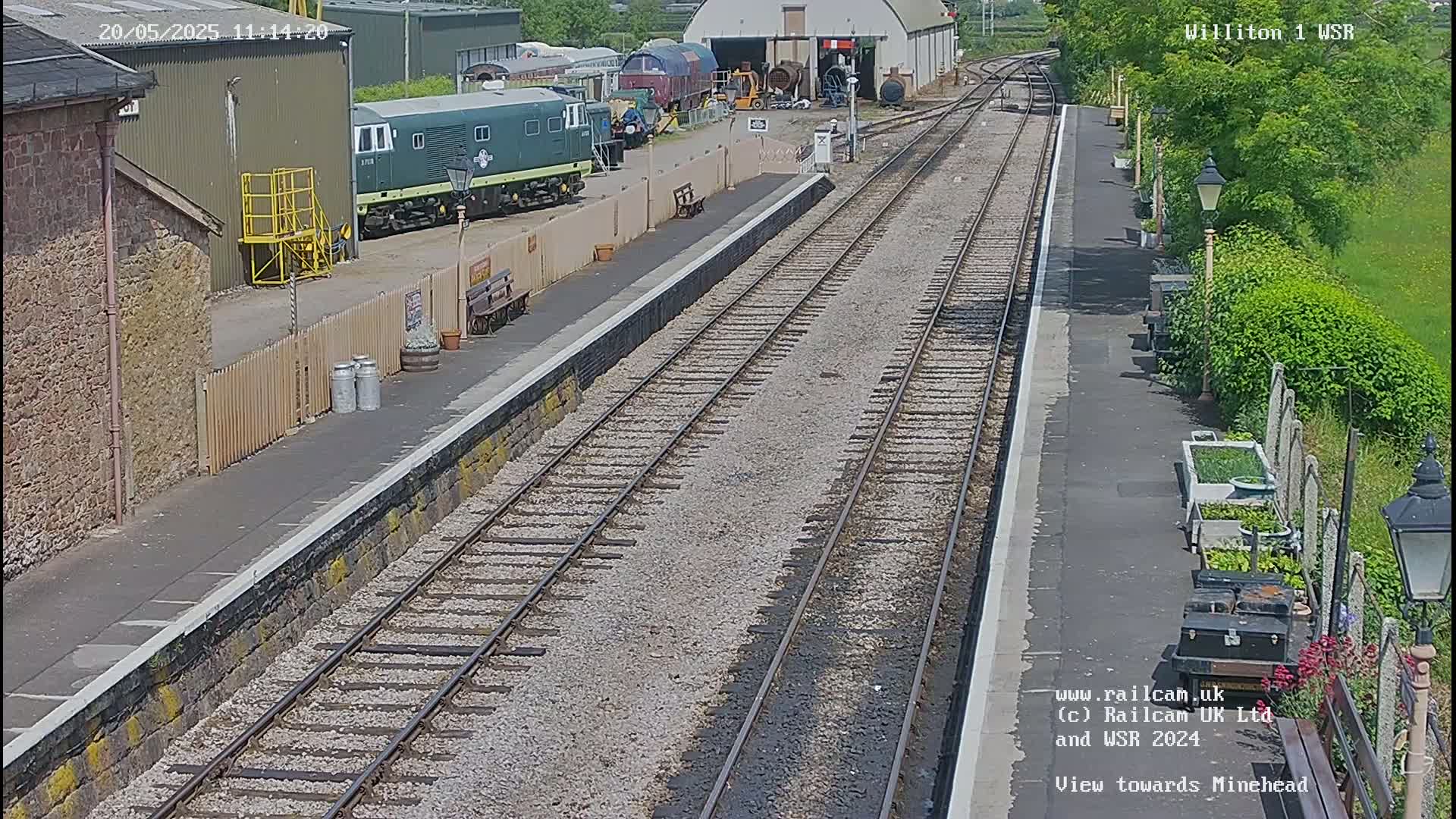 A train station platform with several train cars and railway tracks, on a sunny day.