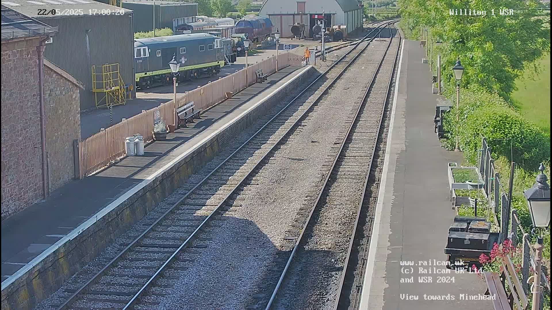 A sunny view of a train station with multiple train tracks, railway buildings, and parked trains.