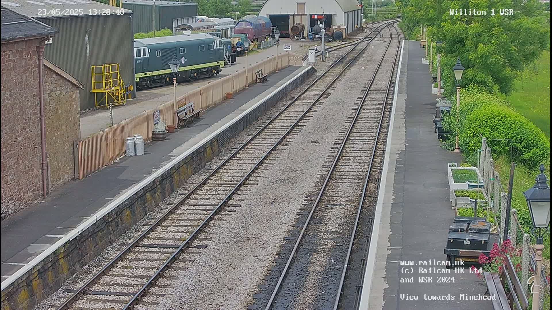 A train station platform with several train cars visible, under a partly sunny sky.