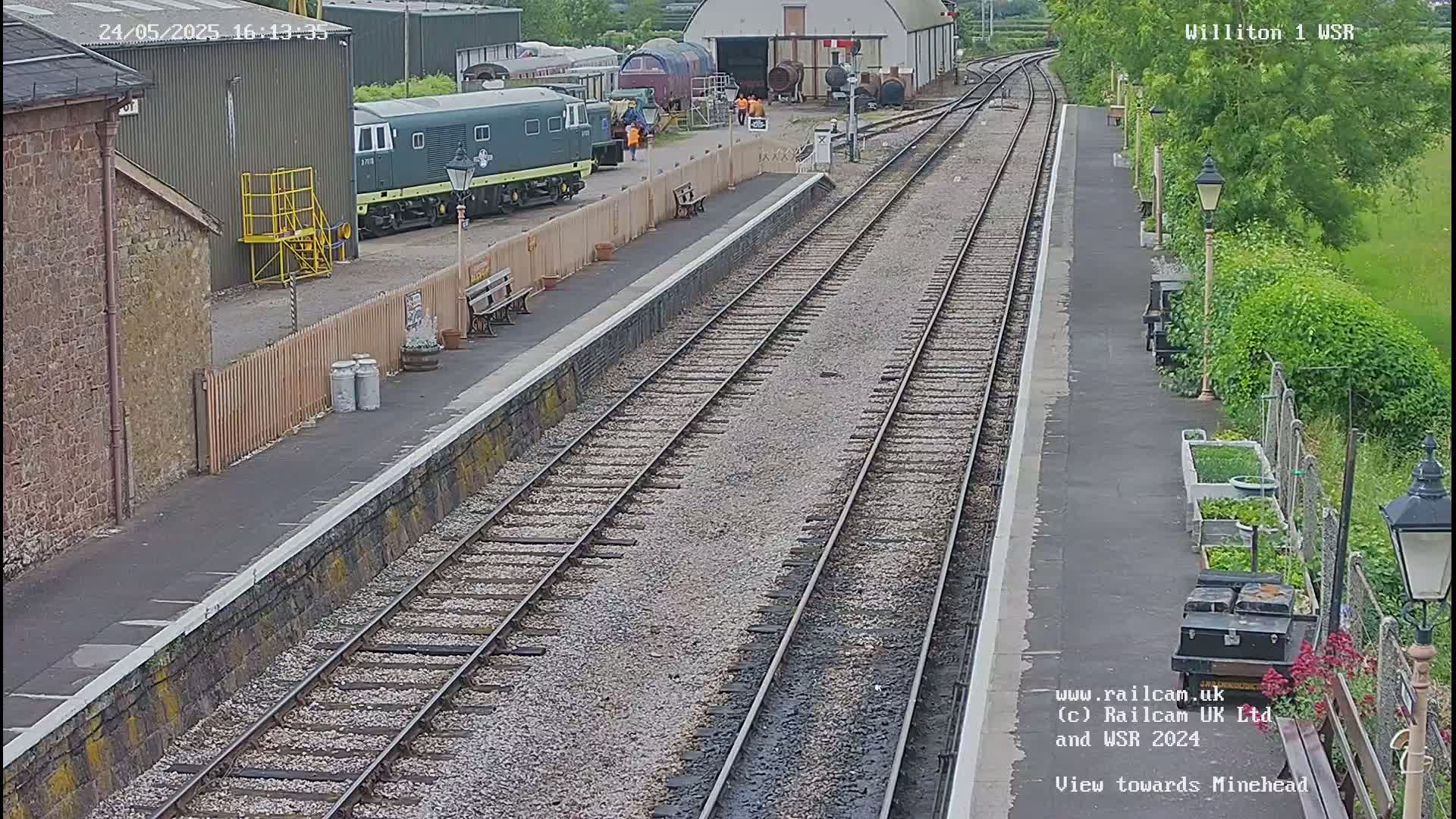 A train station platform with multiple train tracks extending into the distance on a partly sunny day.