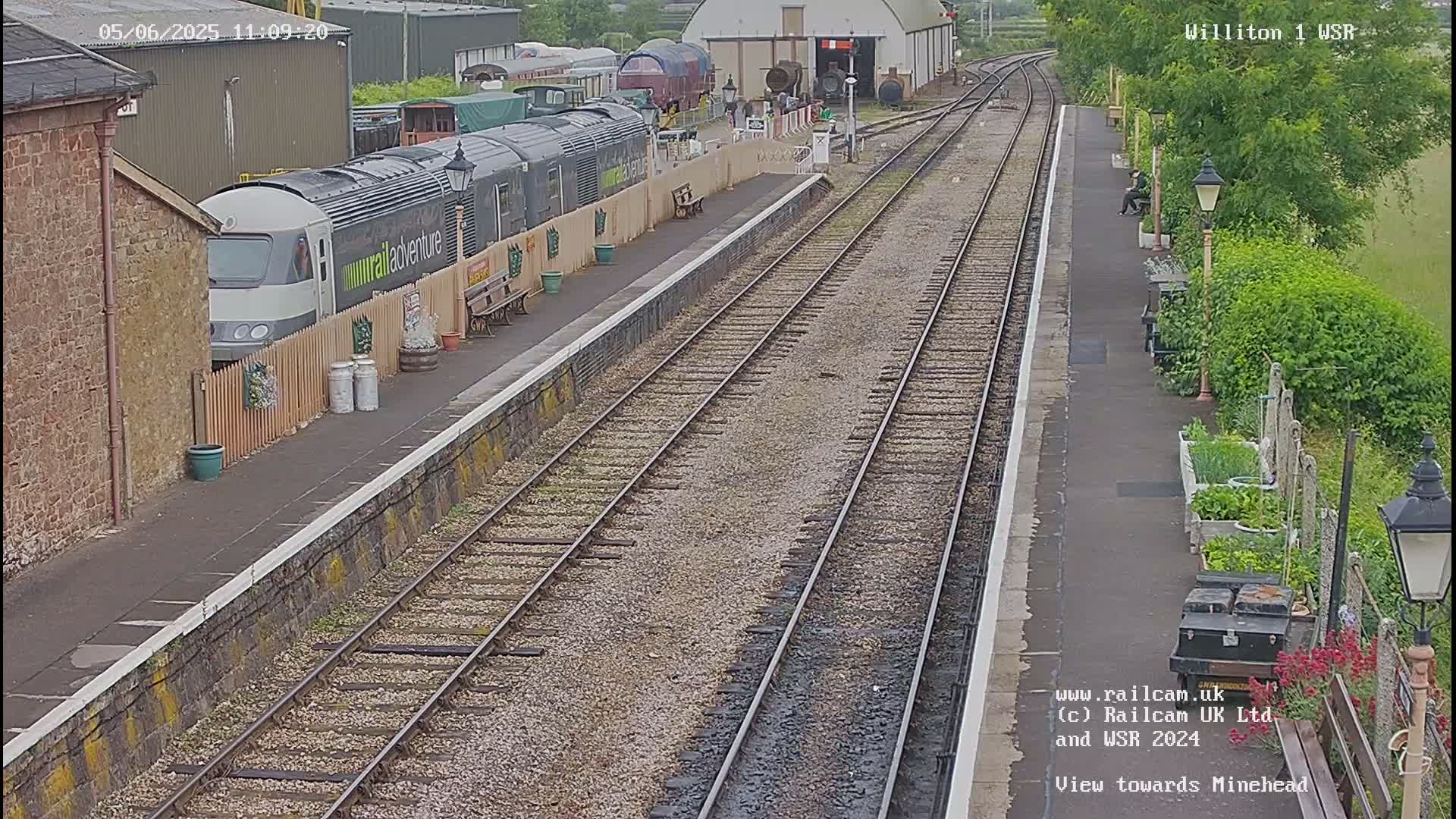 A train sits at a station platform next to railway tracks on an overcast day.