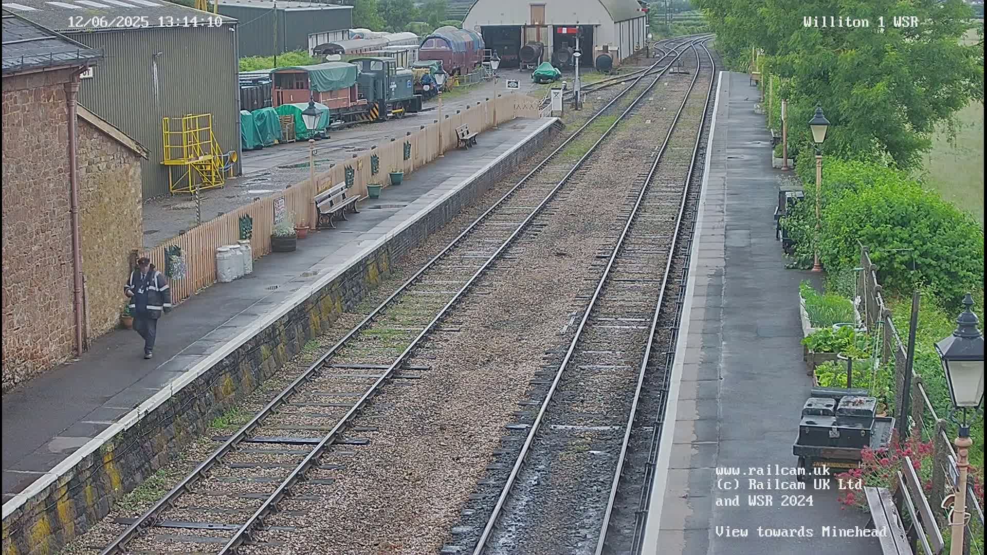 A person walks along a train platform next to railway tracks on an overcast day.