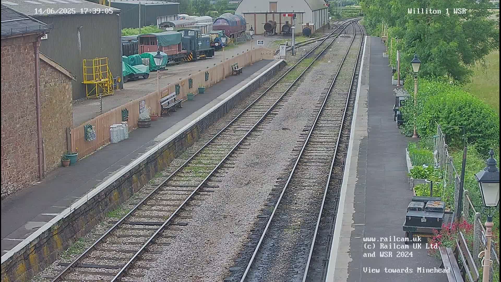 A railway station platform with multiple train tracks and several trains parked nearby on a partly sunny day.