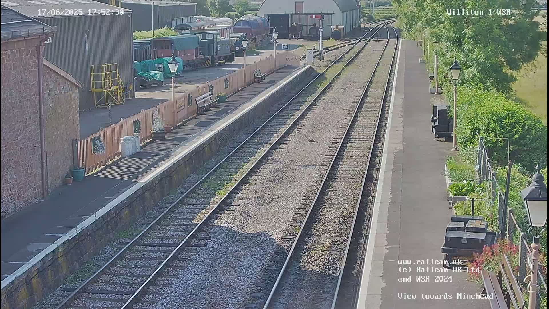 A sunny view of a train station with multiple railway tracks, several train cars, and stone buildings.