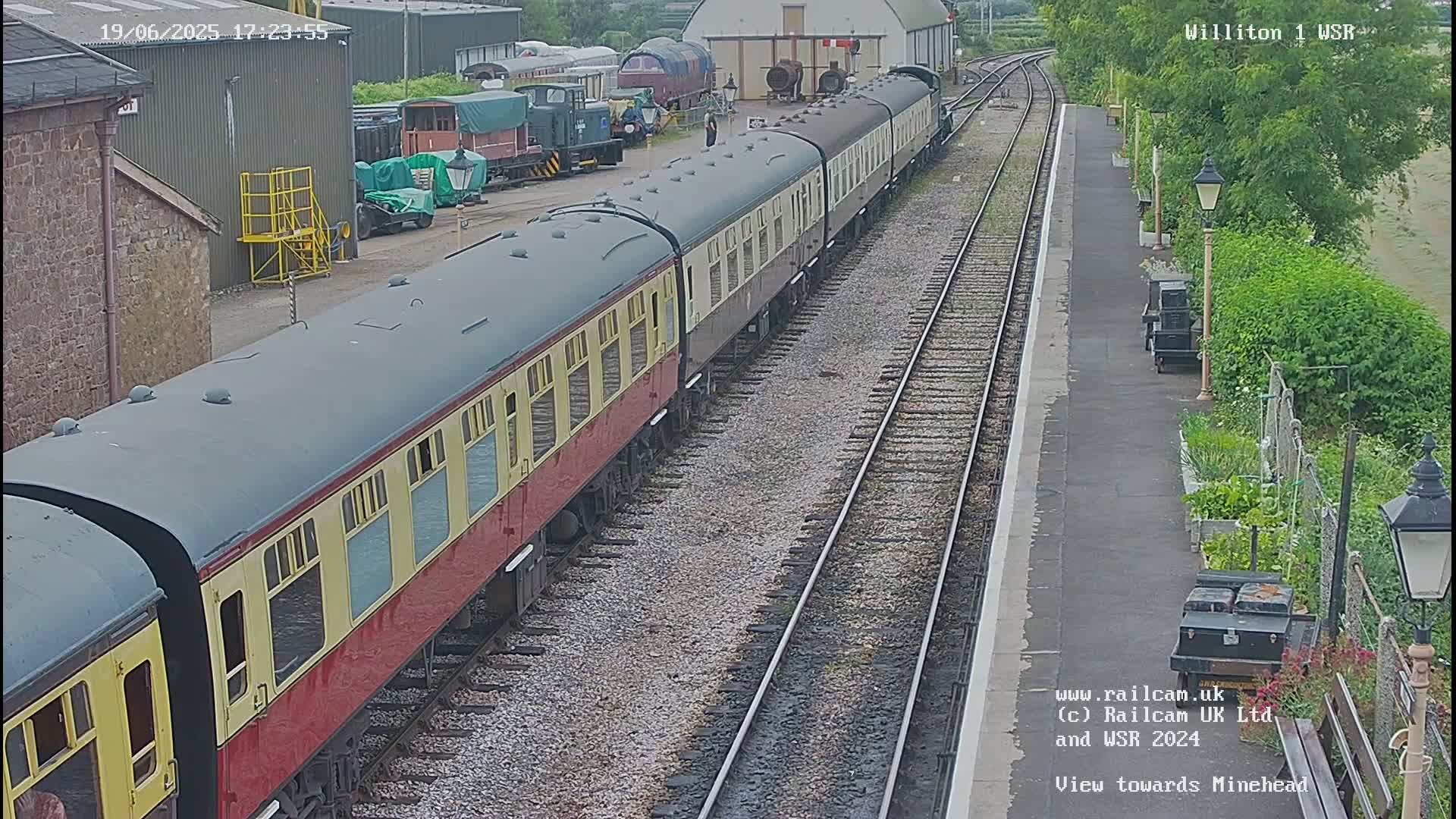 A long passenger train sits at a station on a cloudy day.