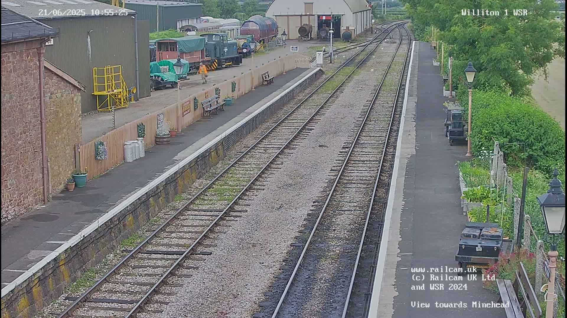 A train station platform with multiple train tracks and several railway cars parked nearby on a partly cloudy day.