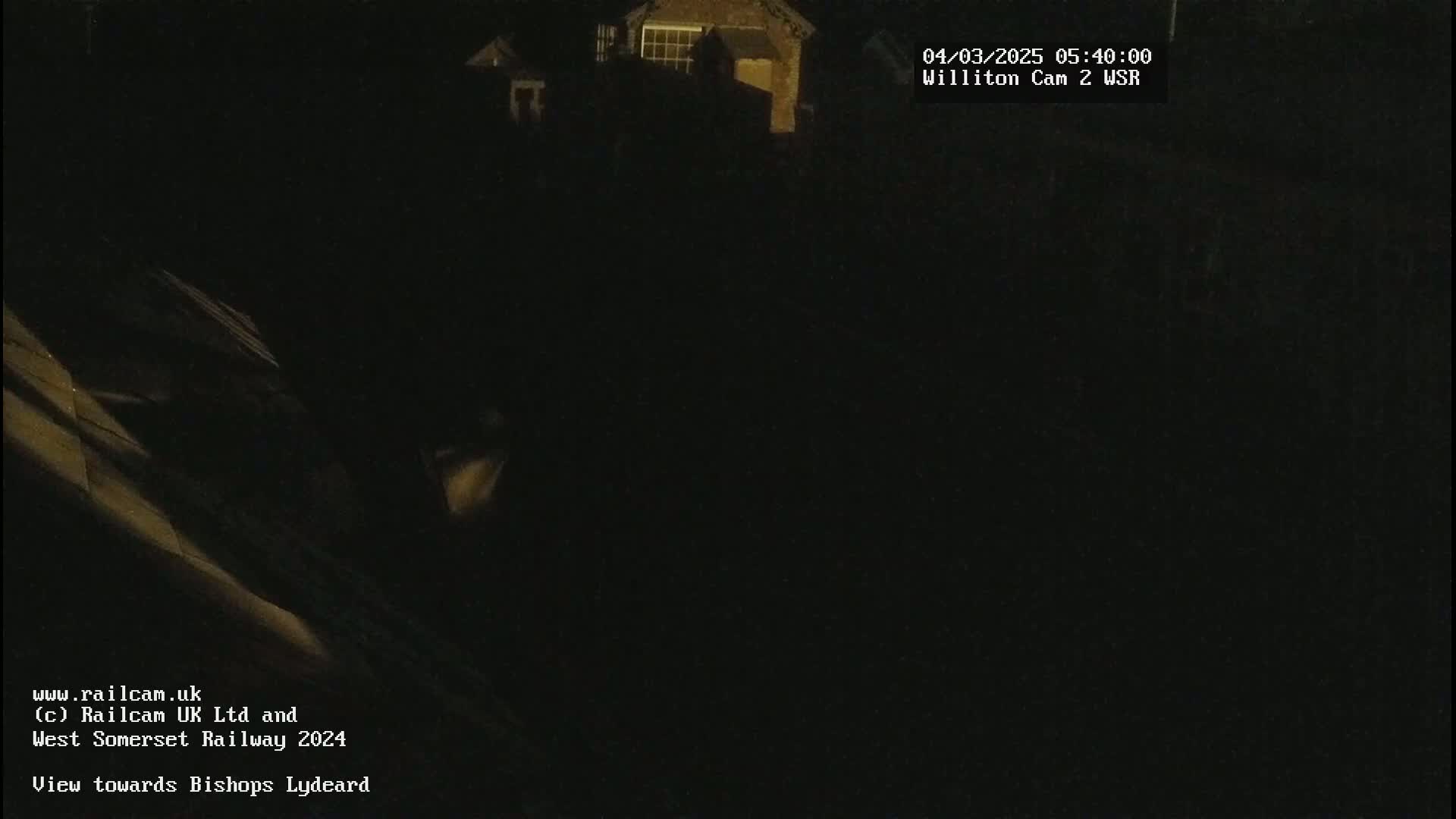 A dark, nighttime view of a building, possibly a house, with some faint light illuminating part of a sloped surface in the foreground.