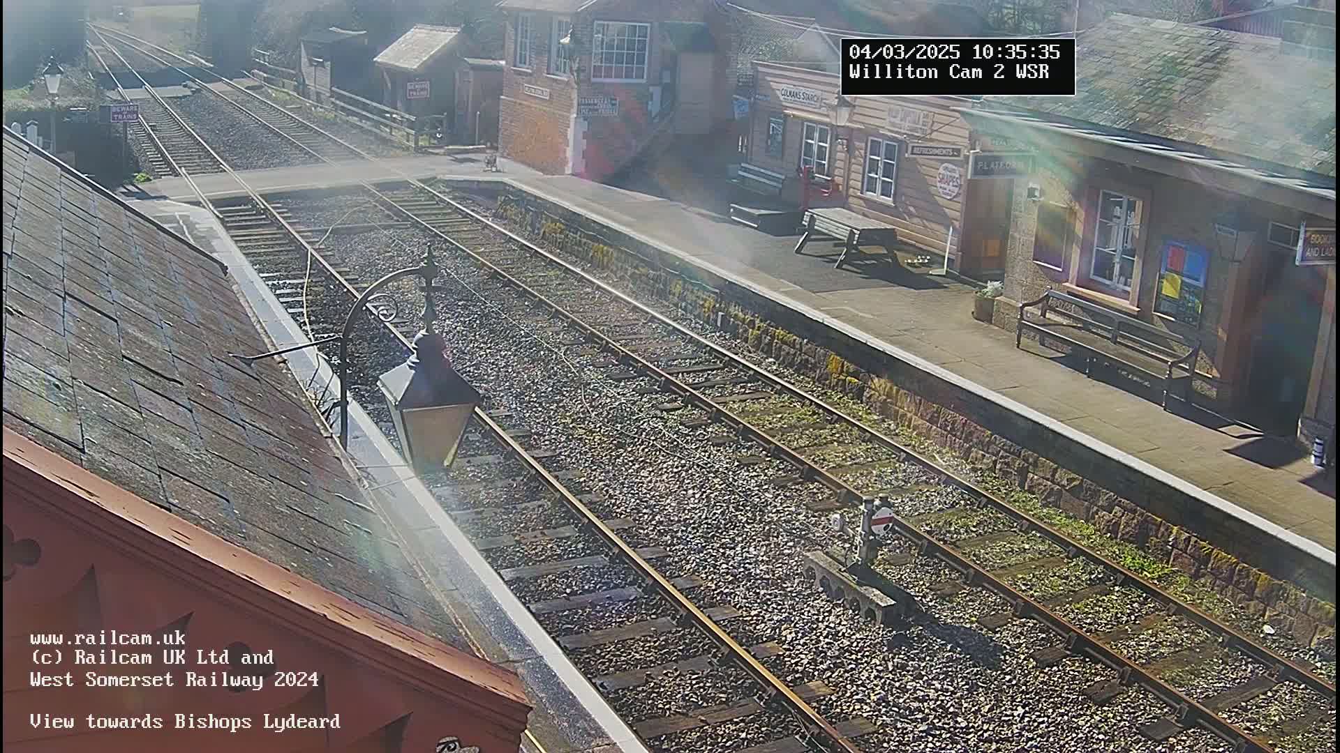 A sunny view of a train station with two parallel train tracks extending into the distance.