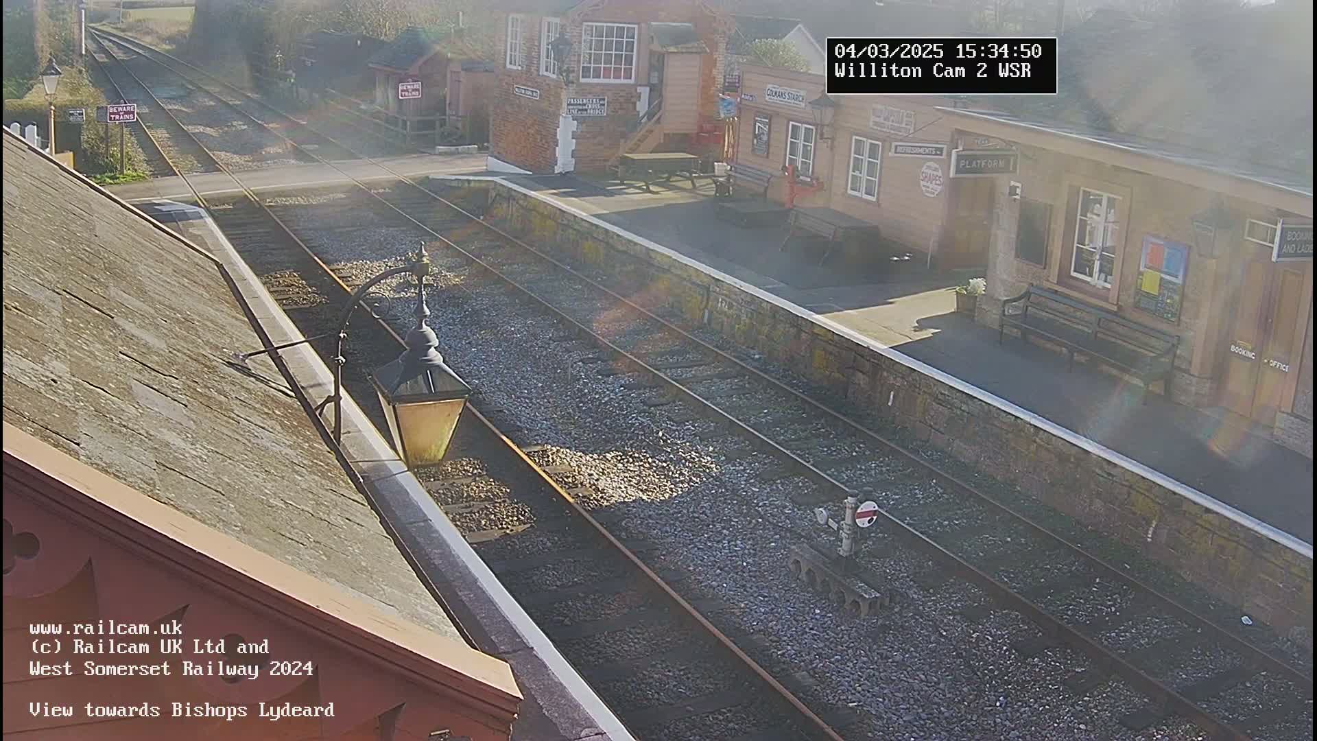 A sunny view from a rooftop overlooking a train station platform and railway tracks.