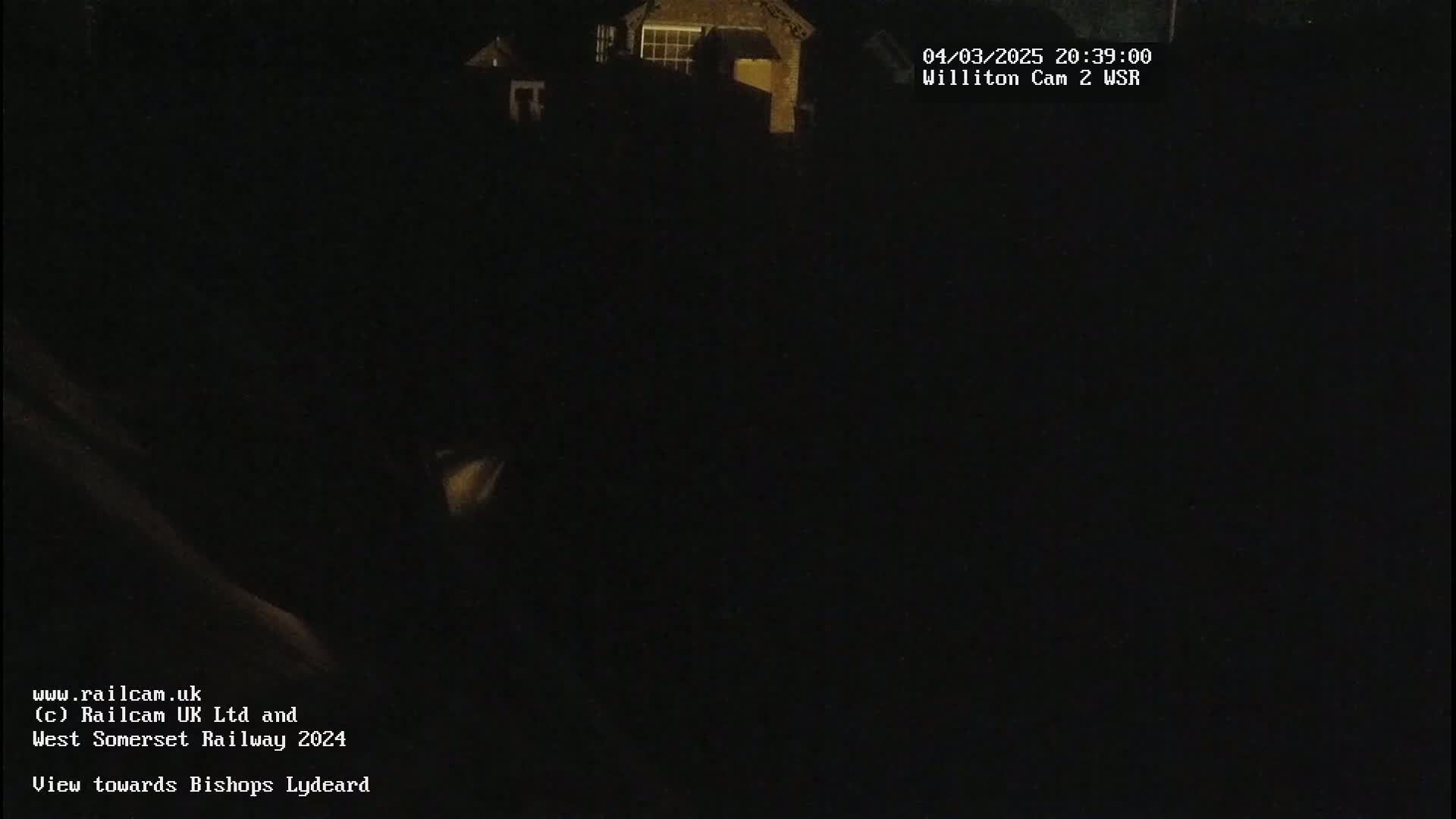 A dark nighttime scene shows a dimly lit building in the distance.