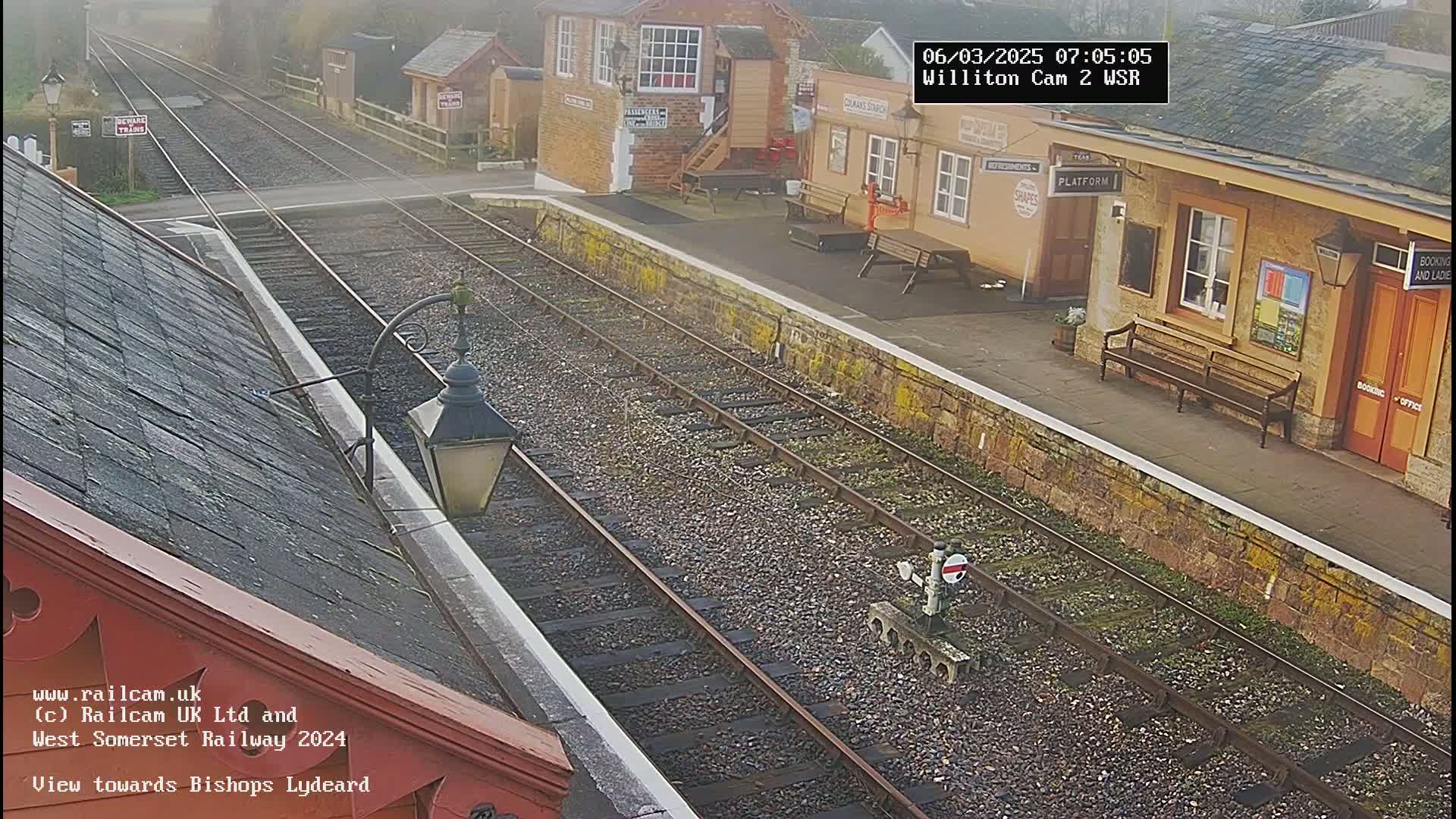 A misty view of a train station platform with two sets of train tracks and a building.