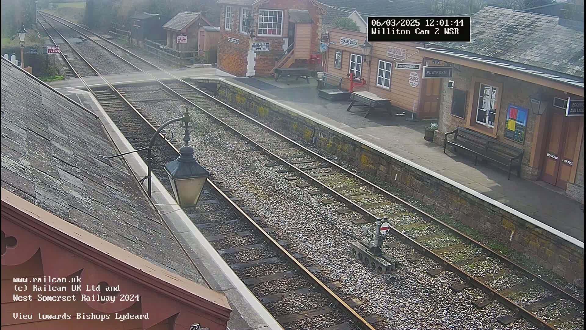 A train station with multiple train tracks and several buildings under an overcast sky.