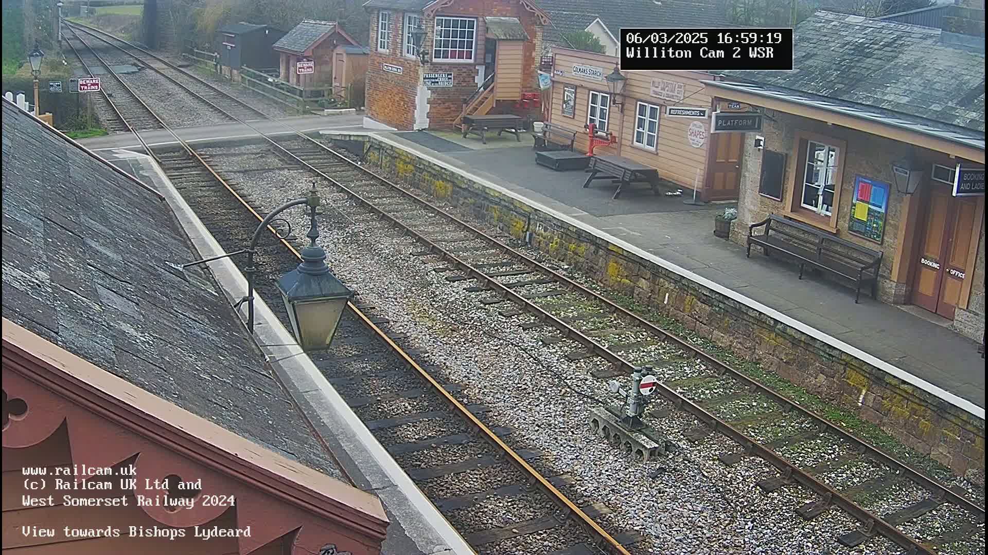 A view of a train station platform with two sets of train tracks on a cloudy day.