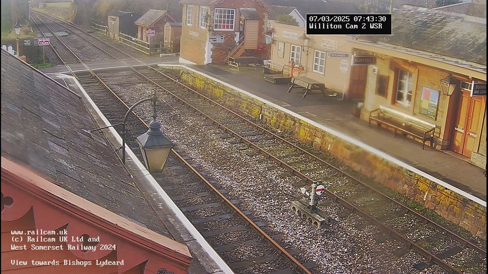A sunny view of a train station platform with railway tracks extending into the distance.