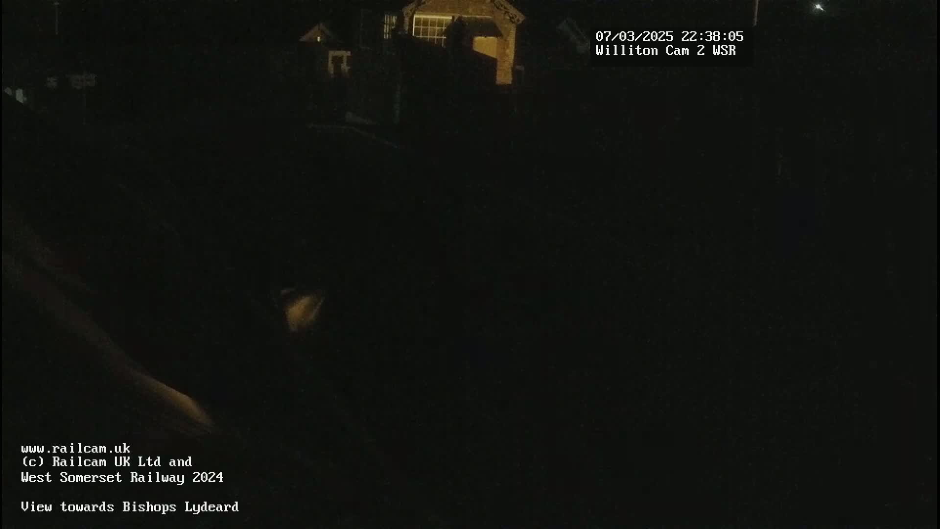A nighttime, low-light view of a dimly lit area, possibly a residential neighborhood, shows some buildings in the distance.