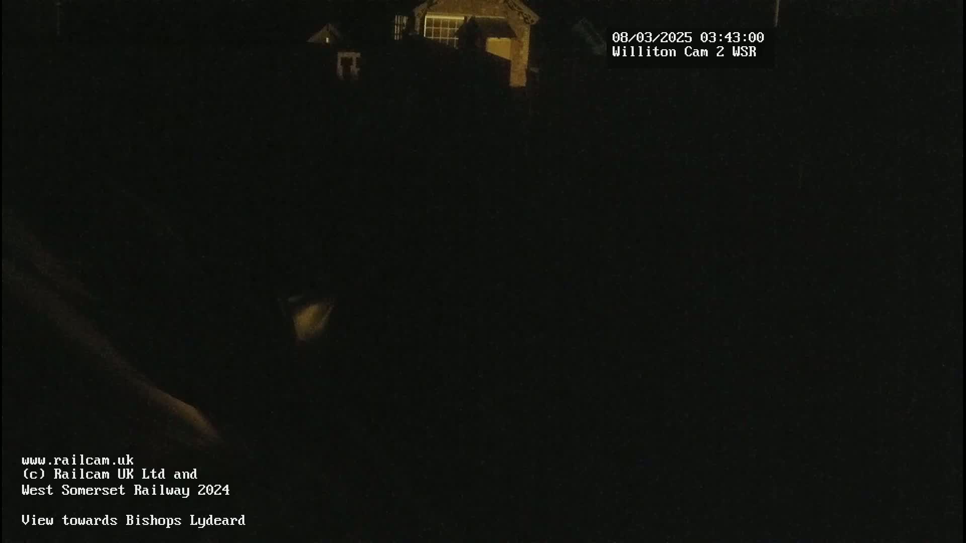 A dark nighttime view shows a dimly lit building in the distance.