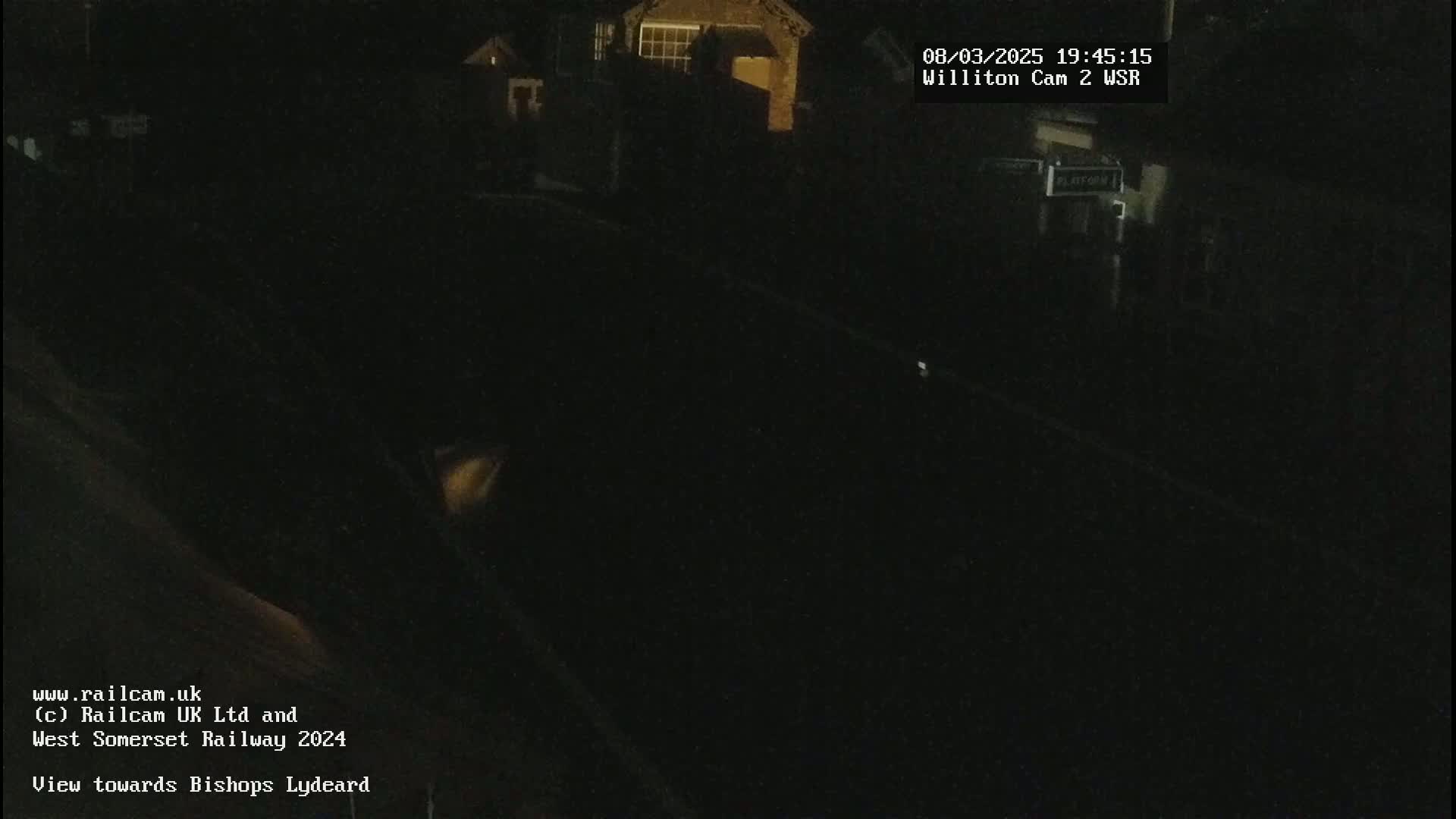 A nighttime, low-light view of a dark railway track and buildings in the distance.