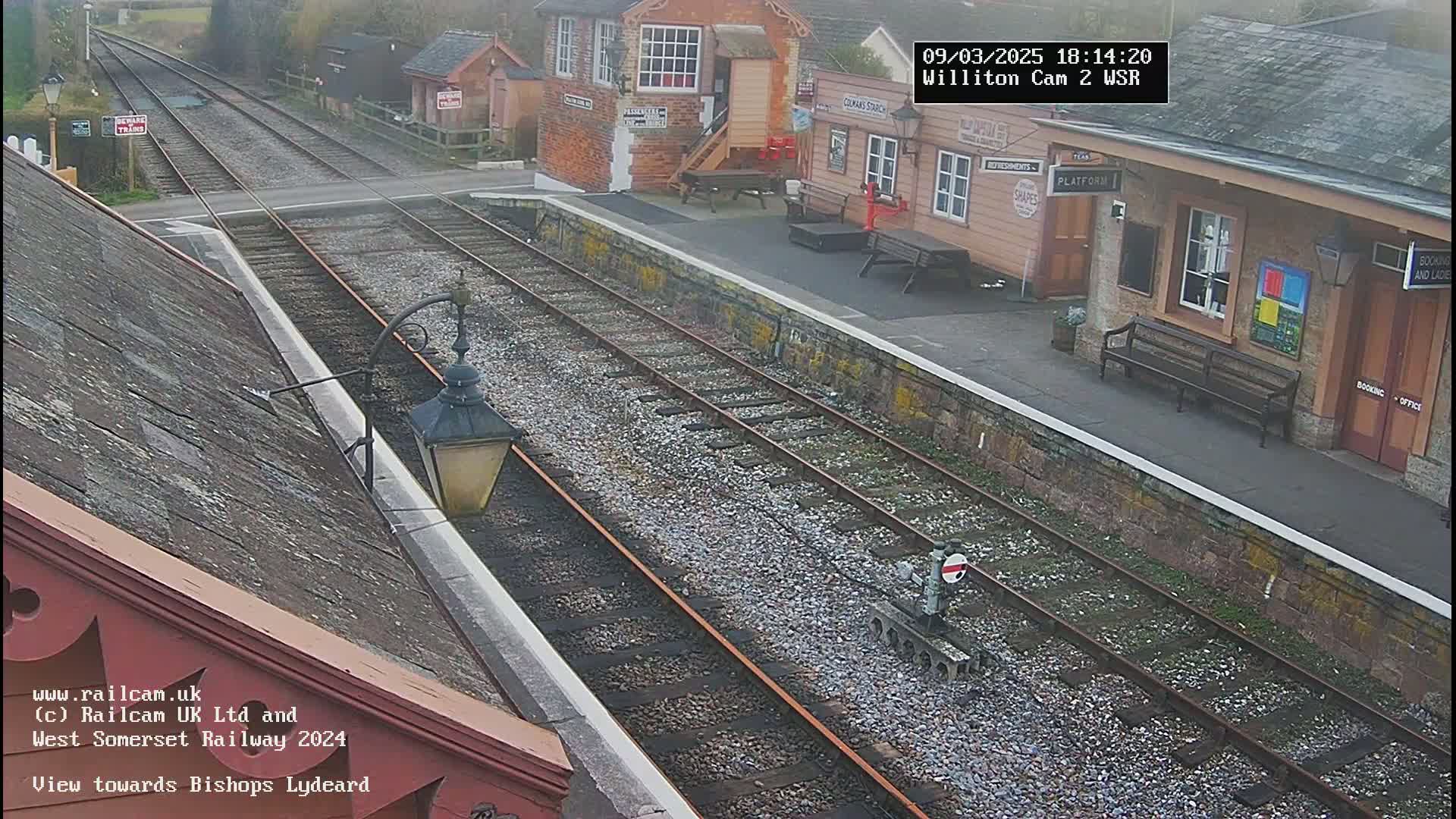 A train station platform with two sets of train tracks extending into the distance under an overcast sky.