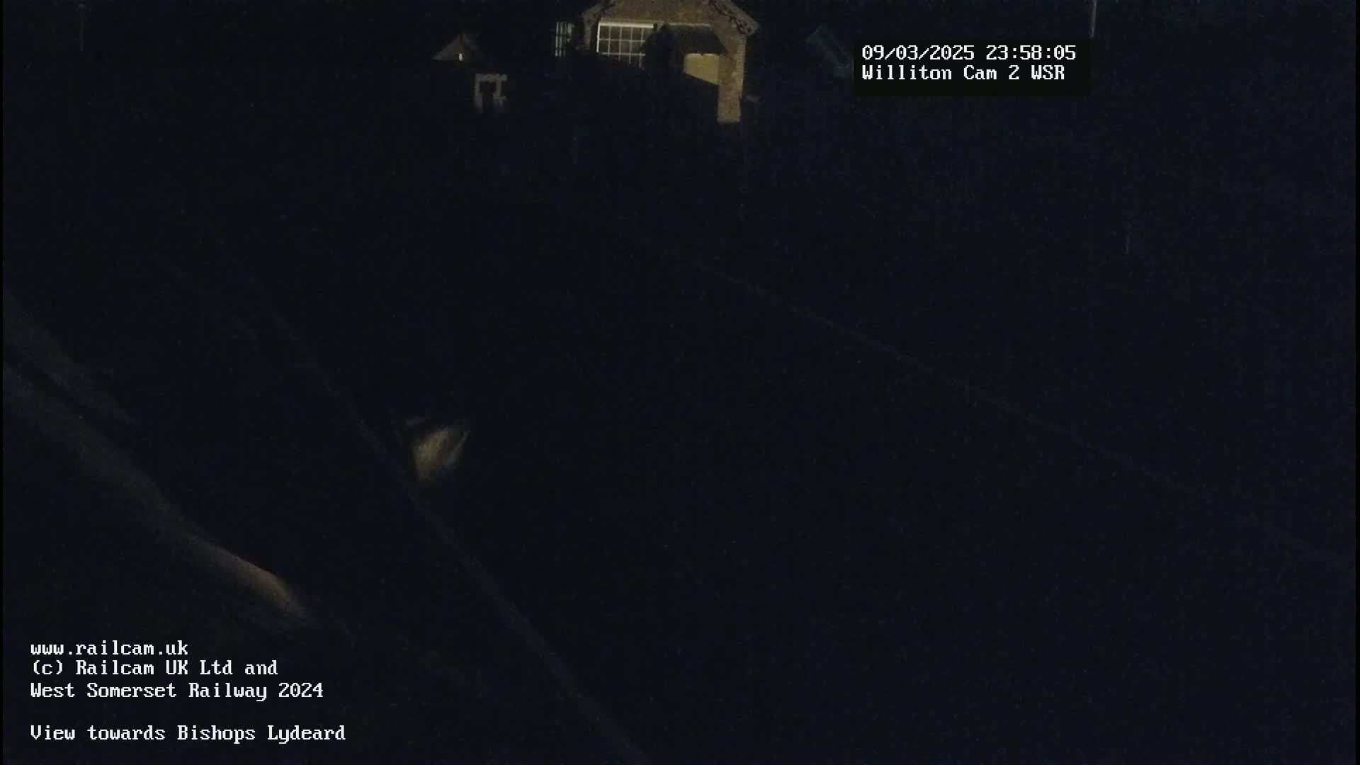 A nighttime, dark view of a railway line, with a building faintly visible in the background.